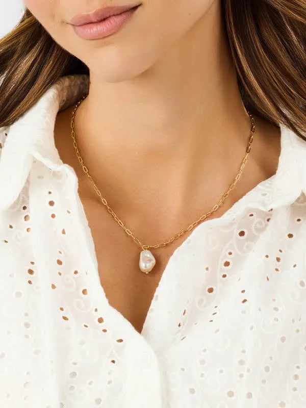Gold necklace with a pearl pendant worn by a person in a white blouse.