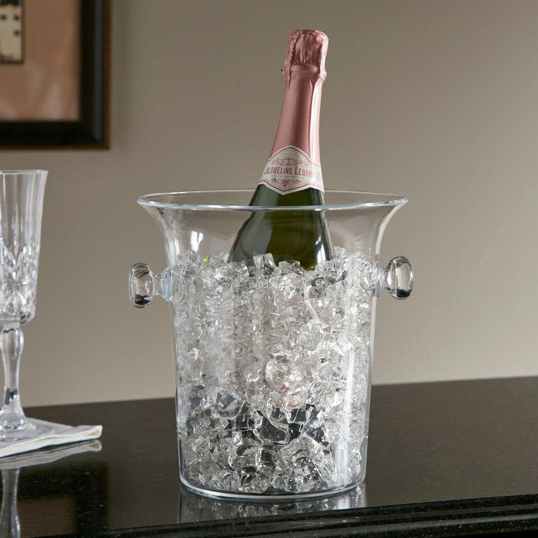 Clear Acrylic champagne ice bucket filled with ice and a bottle of champagne sitting on a table 