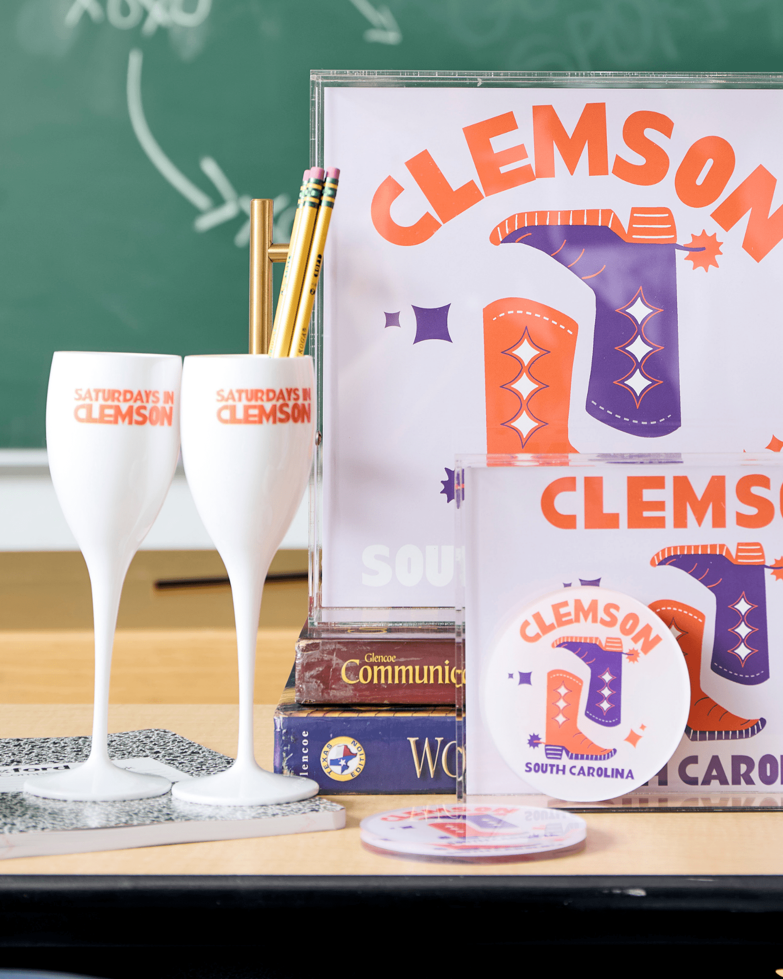 Gameday - Champagne Flute - Acrylic - Saturdays In Clemson- white champagne flute with words Saturdays in Clemson in Orange - photo is product along with coordinating products on a desk with chalkboard background 