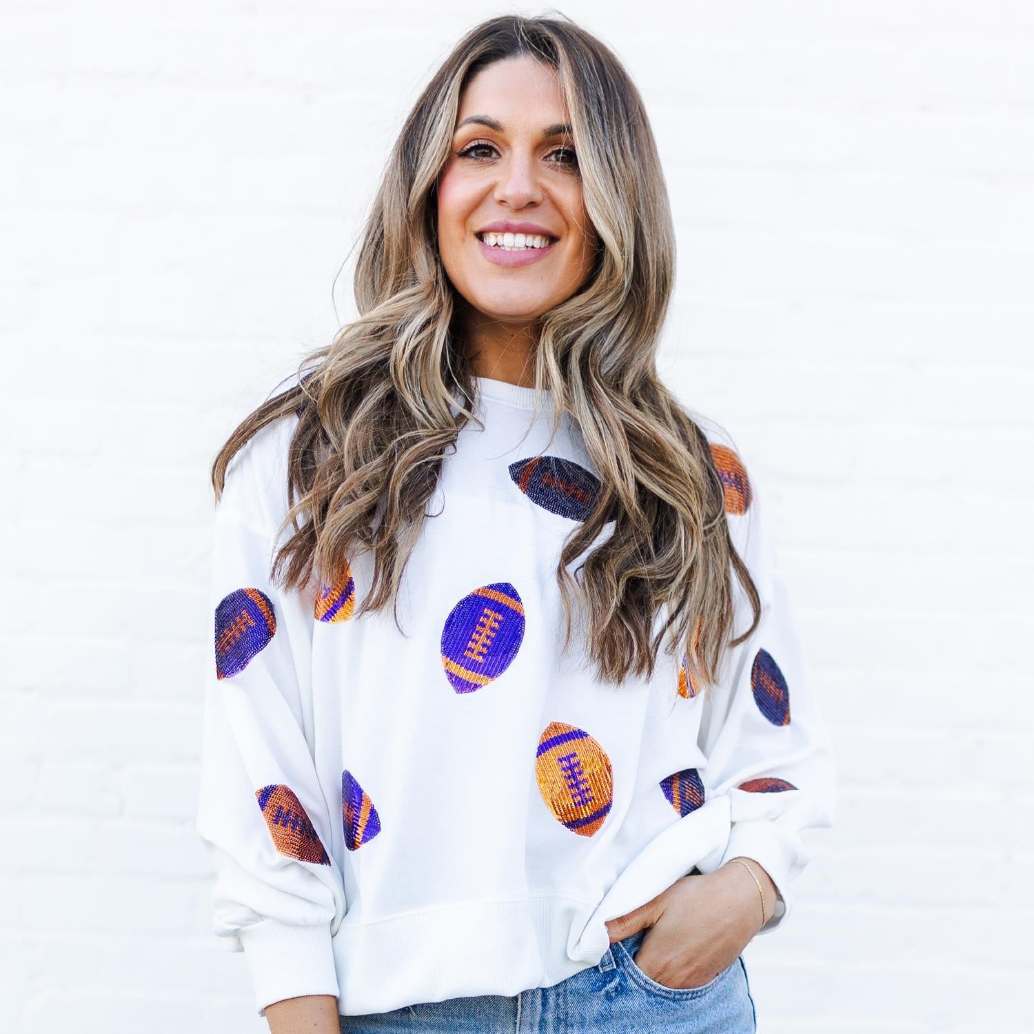 Woman wearing a white sweatshirt with colorful football patterns on a plain background