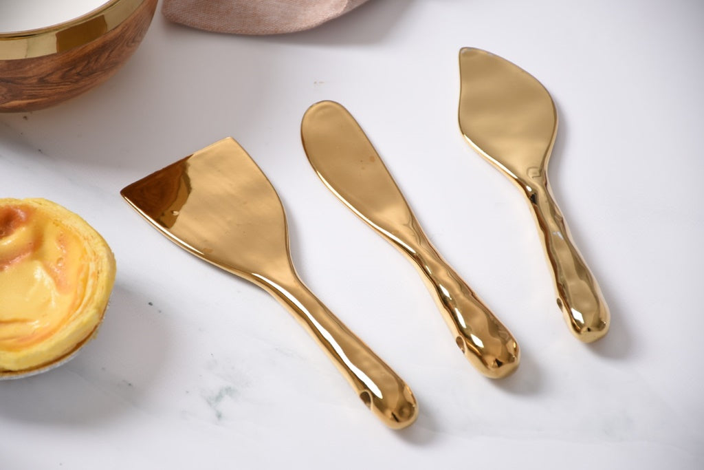 Set of gold cheese knives on a marble surface with a bowl of cheese.