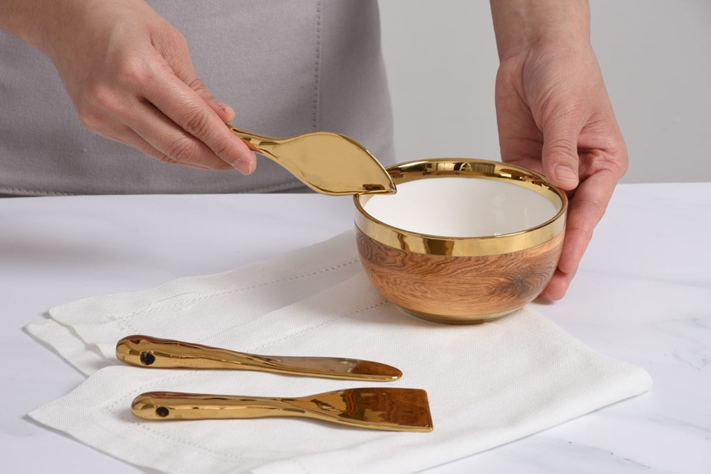 Wooden bowl with gold rim and matching spoons on a white surface