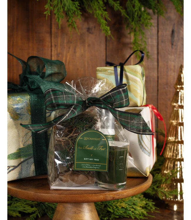 Seasonal - Smell of tree Gift Set showing candle, spray and potpourri that make up the set.  Tied in a clear bag with a green plaid bow. Photo shows product on a cake stand with other holiday themed items 