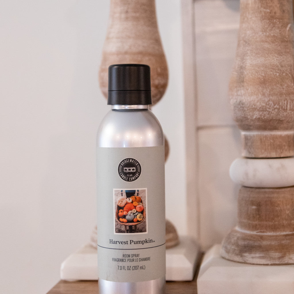 Seasonal - Room Spray - Harvest Pumpkin scent - silver bottle with gray label.  Product is sitting on a table with wooden candlesticks 