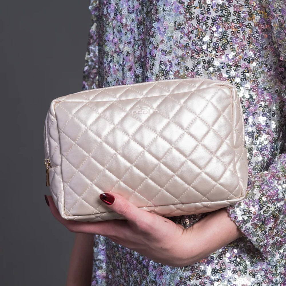 Quilted beige handbag held by a person wearing a sparkling dress.
