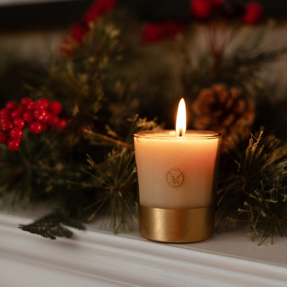 Candle with a gold base in front of Christmas decorations