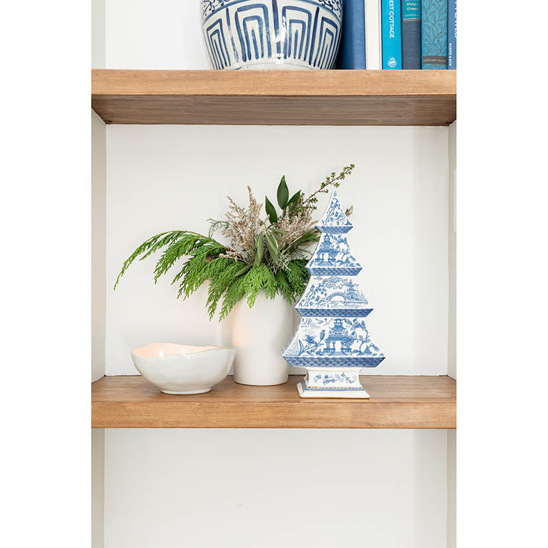 Decorative items on a wooden shelf including a white vase with greenery, a blue and white pagoda, and books.