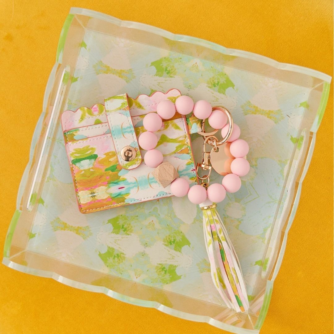 Pink beaded keychain with tassel on a floral card against a yellow background