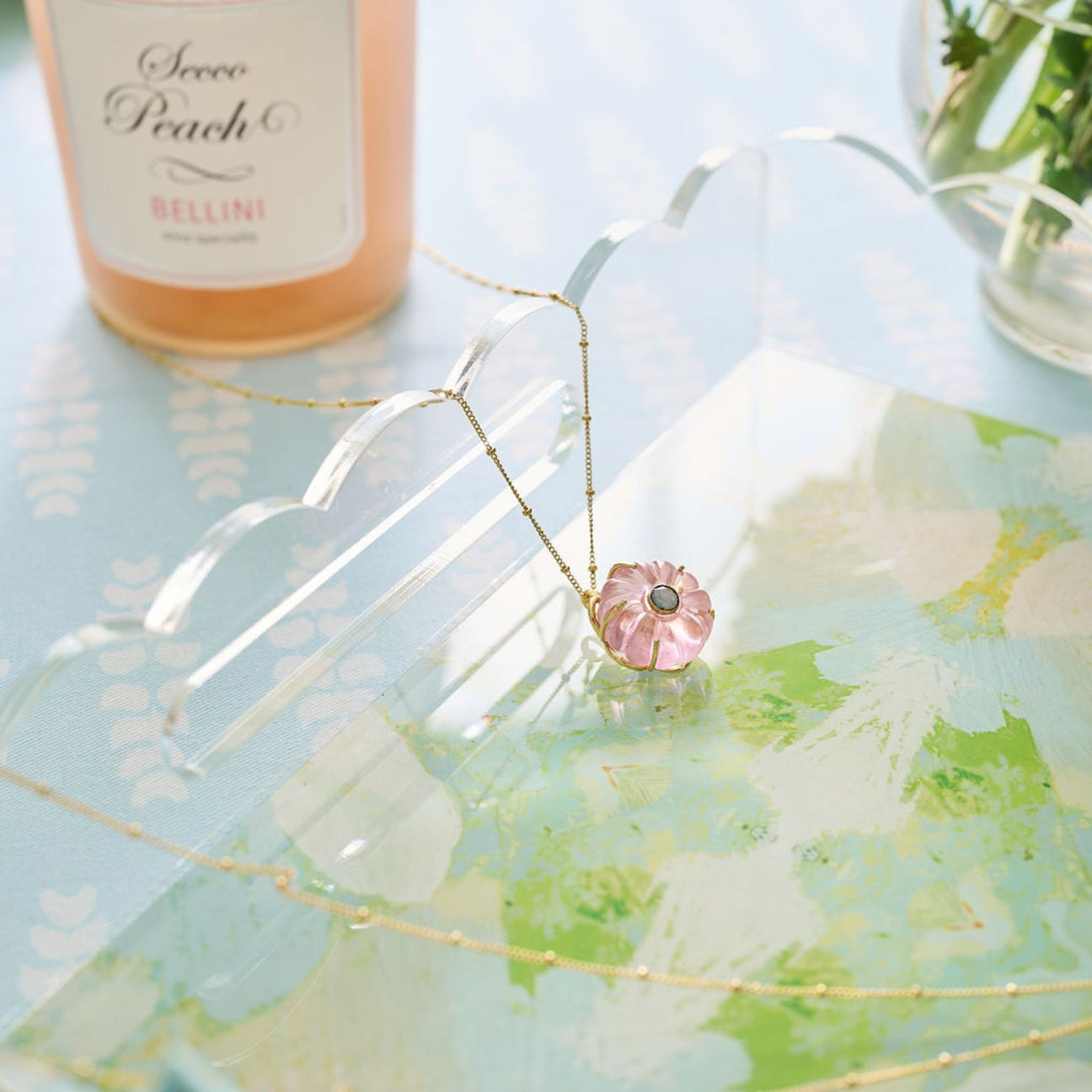 Necklace with a pink pendant on a decorative acrylic tray with a world map design.
