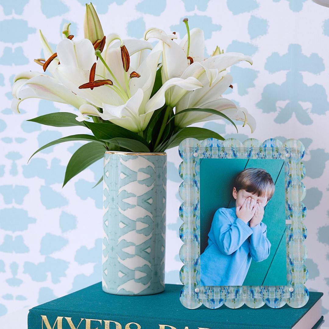 Vase with white lilies and a photo frame on a book against a patterned background