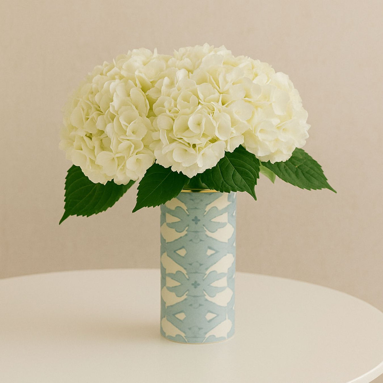 White hydrangeas in a patterned vase on a beige background