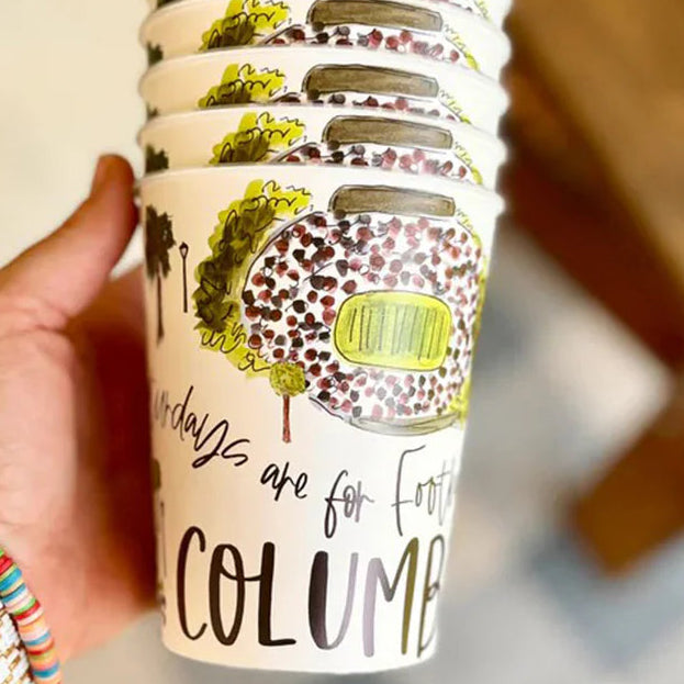 Stack of coffee cups with artistic designs and text, held by a hand.