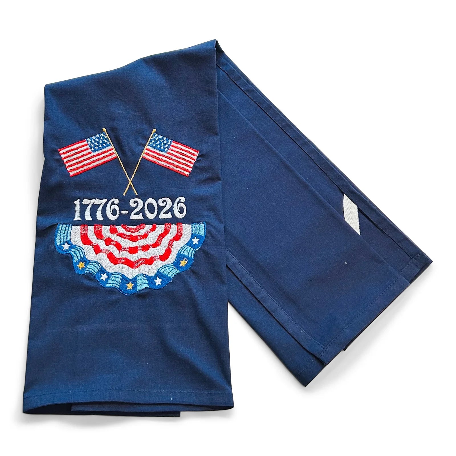 Folded blue towel with American flags and '1776-2026' text on a white background