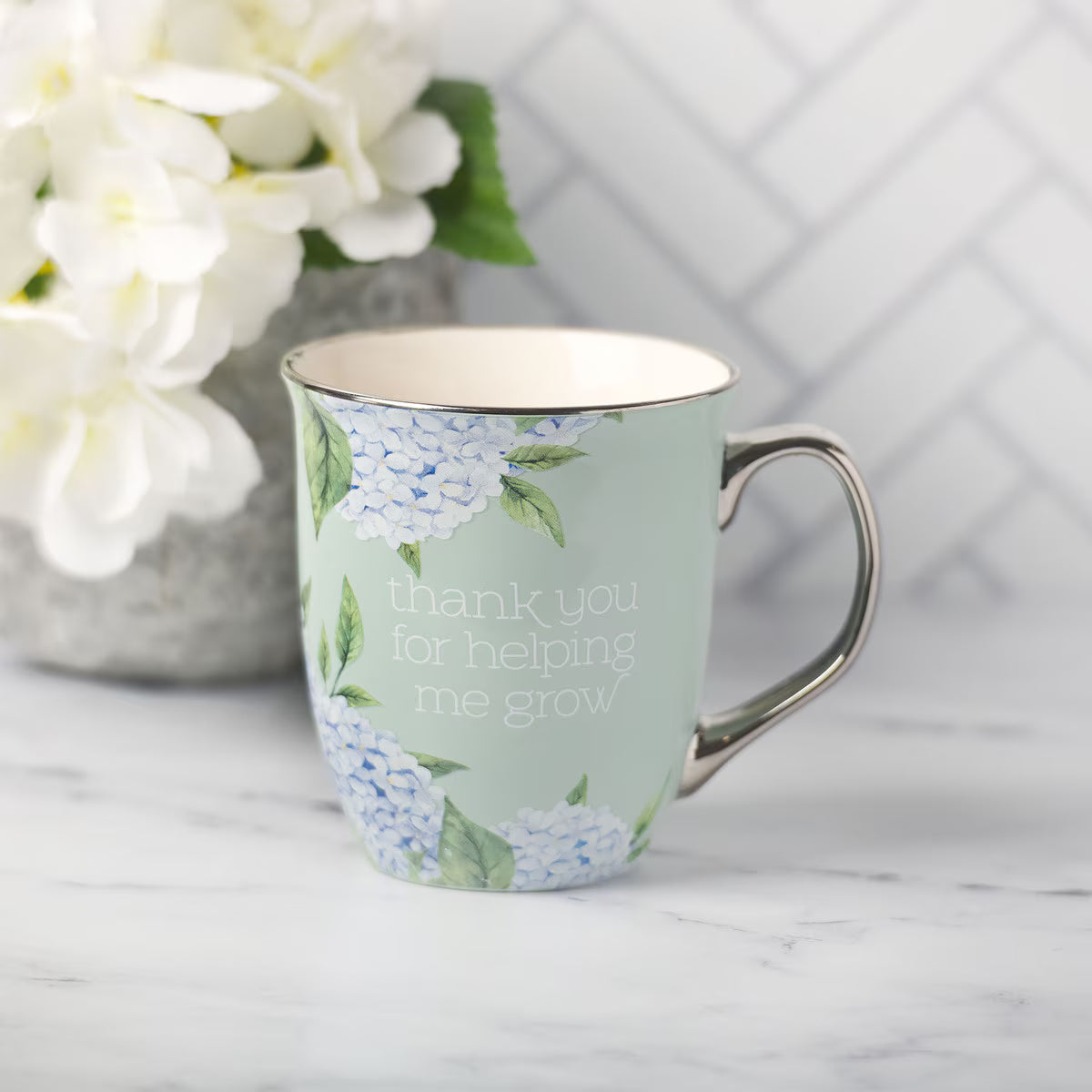 Mug with floral design and text 'thank you for helping me grow' on a marble surface with flowers in the background.