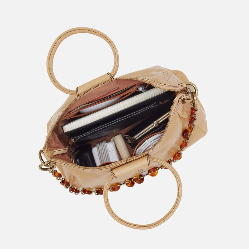 Beige handbag with circular handles, open to reveal its contents on a light beige background