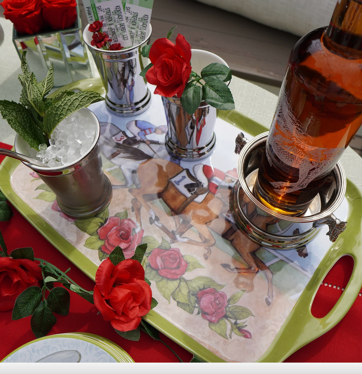 Green trimmed melamine horse racing decorated tray on red cloth with red roses, mint julep cps filled, bottle of bourbon