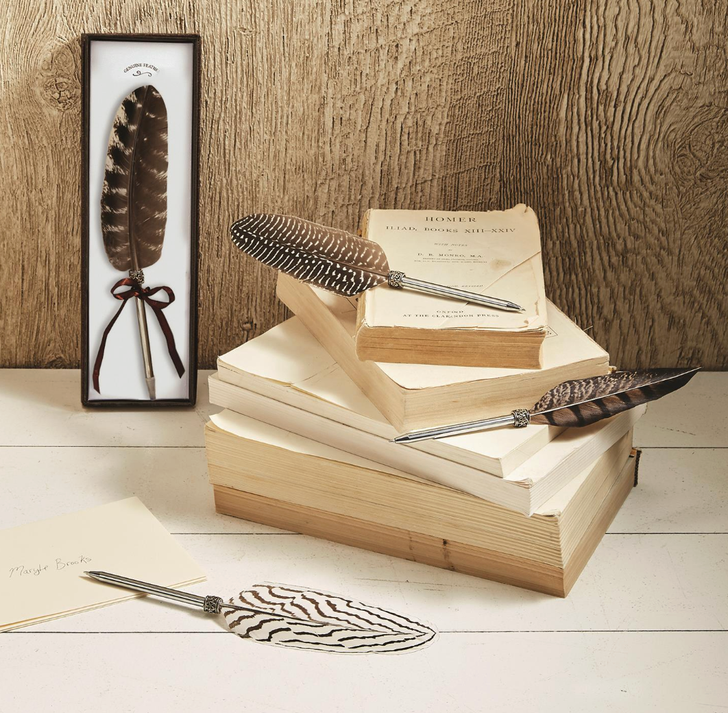 Stack of books with assorted colors of brown and white refillable natural feather pens on a wooden surface