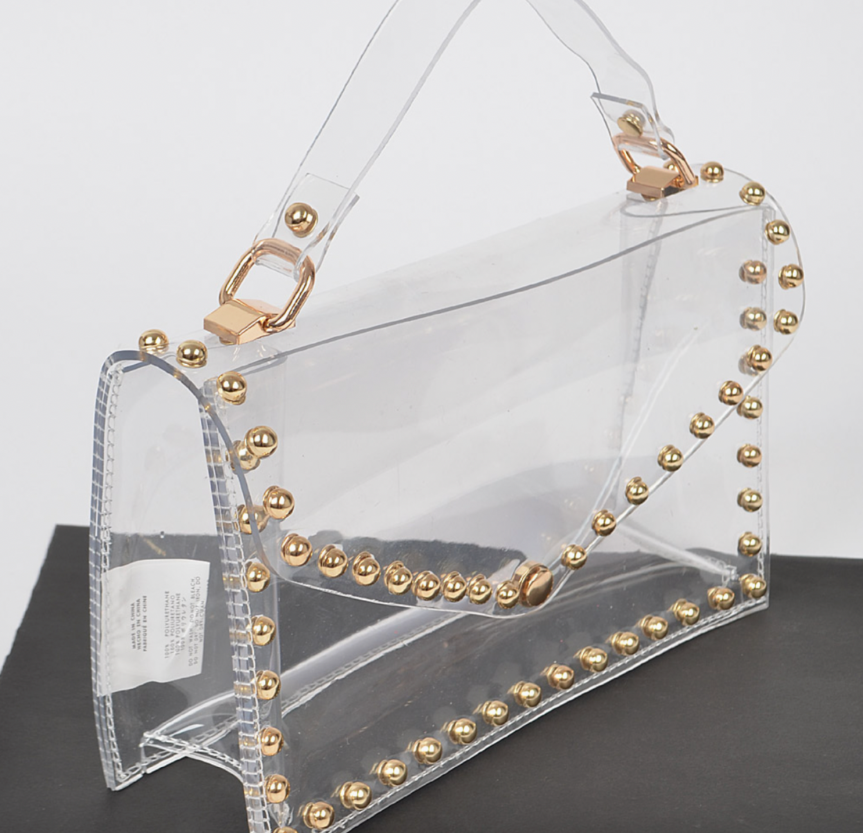 Clear bag with gold studs and gold hardware on white background