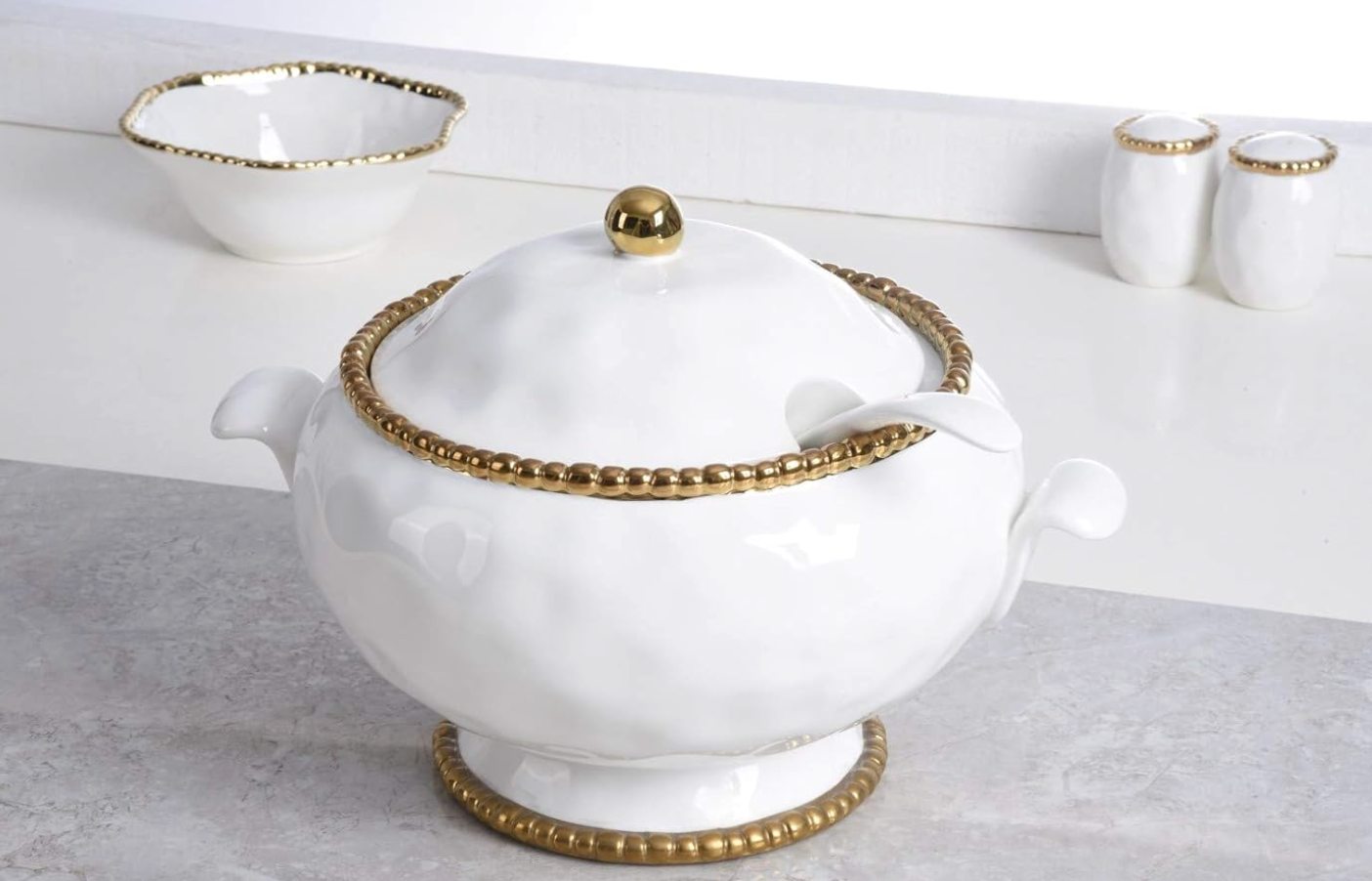 White ceramic and titanium Pampa Bay tureen and spoon with gold accents on a light gray surface.