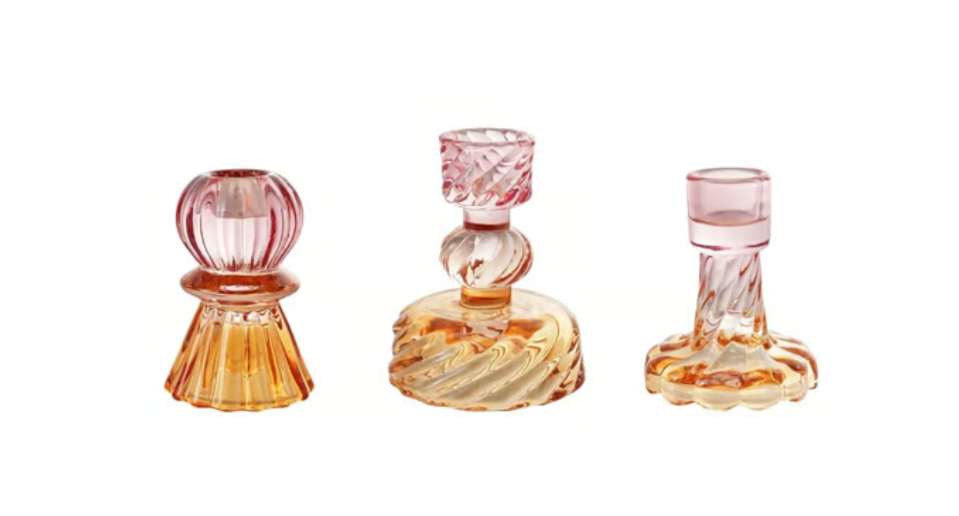 Hazel Mazel set of three two-toned glass taper candle holders in blush pink and warm amber yellow, each with a unique wavy sculptural base — globe, disc, and fluted column silhouettes — on a white background"