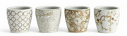 Four white ceramic cachepots with taupe and white floral and geometric patterns, arranged in a row against a white background.