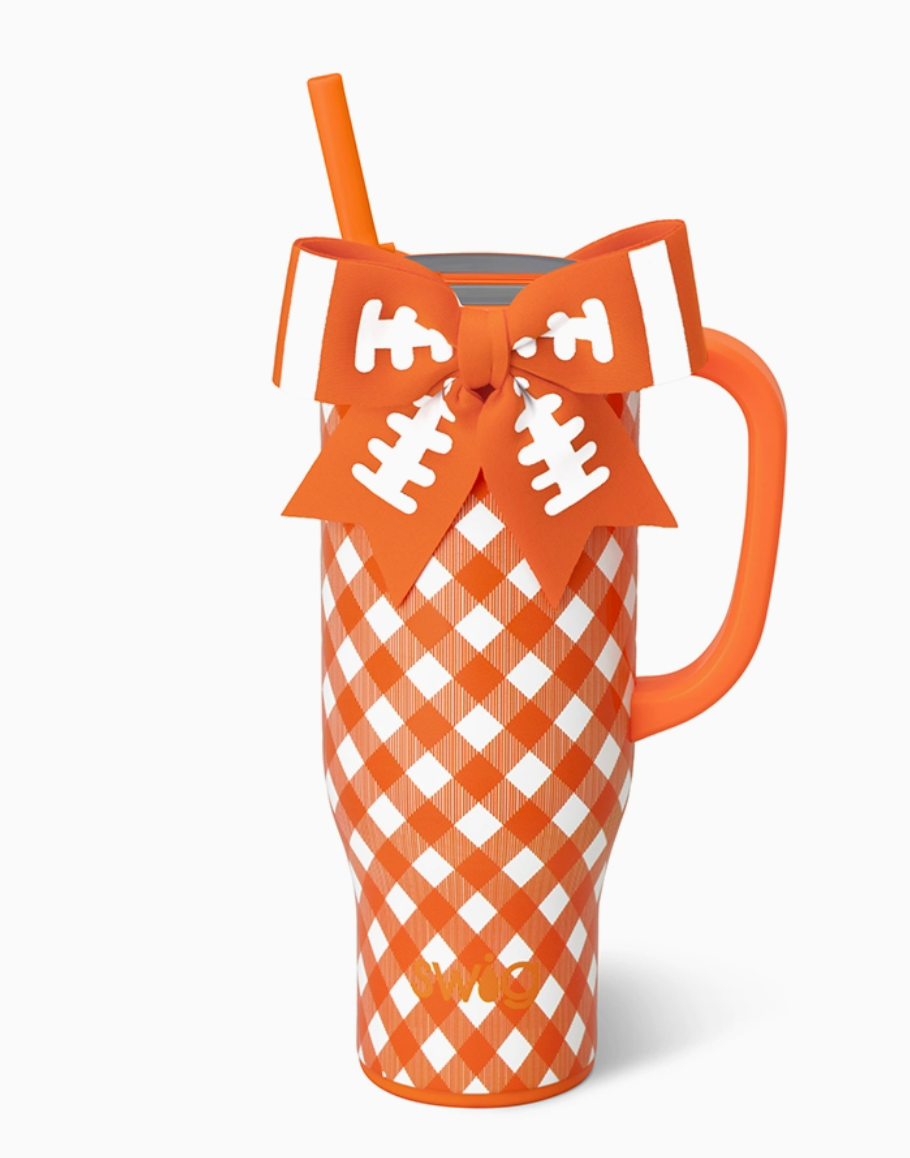 A tall insulated tumbler with an orange and white gingham pattern, an orange handle, and a matching orange straw. A football-shaped ribbon bow with white laces is tied around the upper portion of the tumbler.