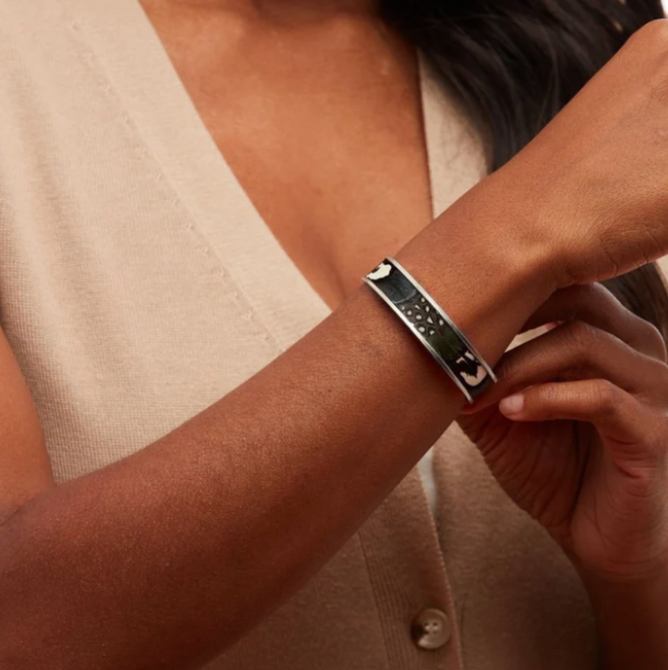 A gold-toned open cuff bracelet featuring black and white feathers set in gold outer band with a photographed on woman's wrist