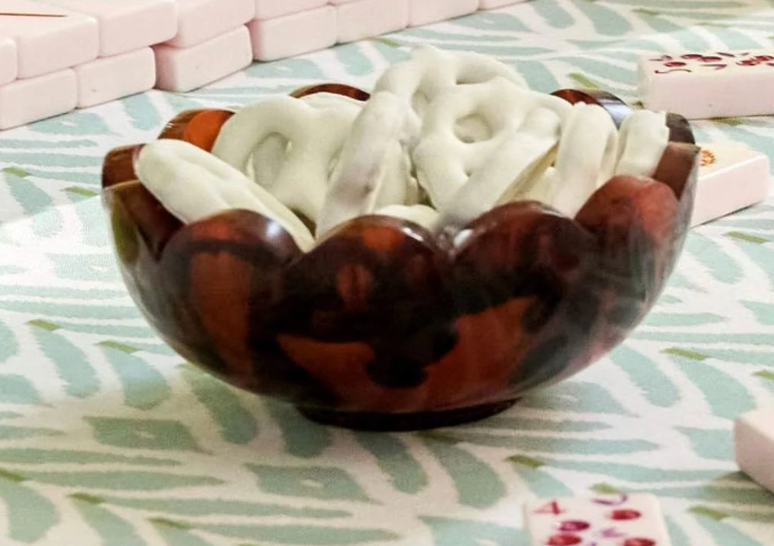 Laura Park brand tortoise shell scalloped edge resin snack bowl filled with white chocolate covered pretzels on pale green patterned cloth and mahjong tiles scattered