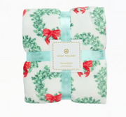  Mary Square brand fleece blanket with a green holiday wreath and red bow print folded in a ribbon package that says Mary Square Fleece Blanket on a white background