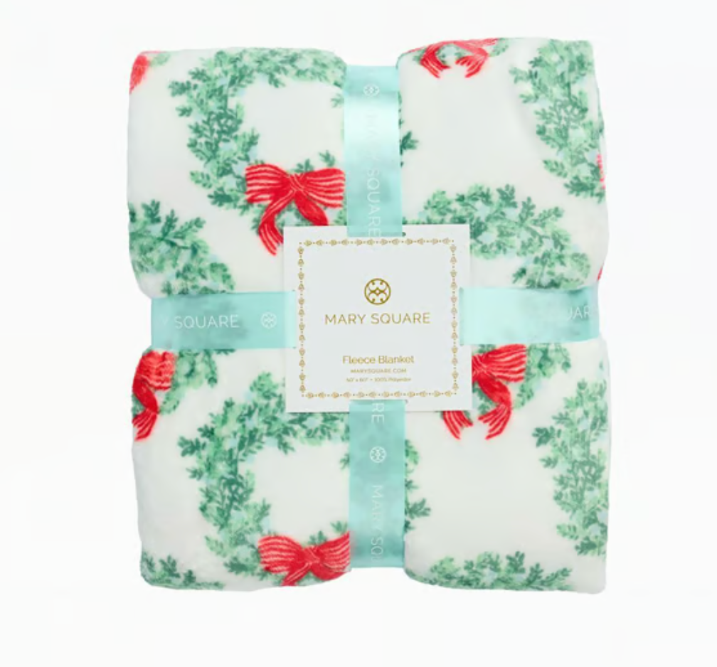  Mary Square brand fleece blanket with a green holiday wreath and red bow print folded in a ribbon package that says Mary Square Fleece Blanket on a white background