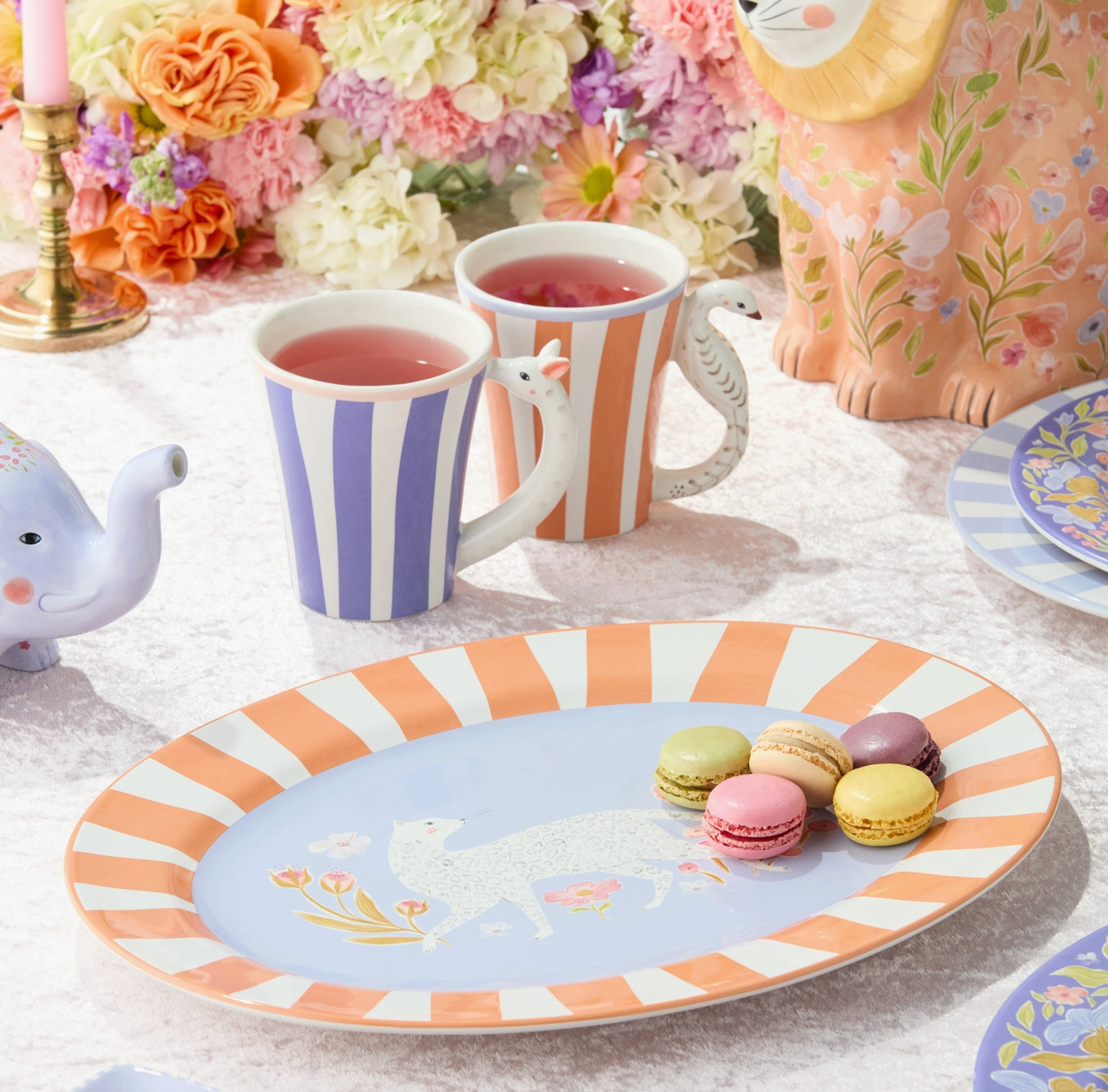 Tea party setup with striped mugs, a plate with macarons, and floral decorations.