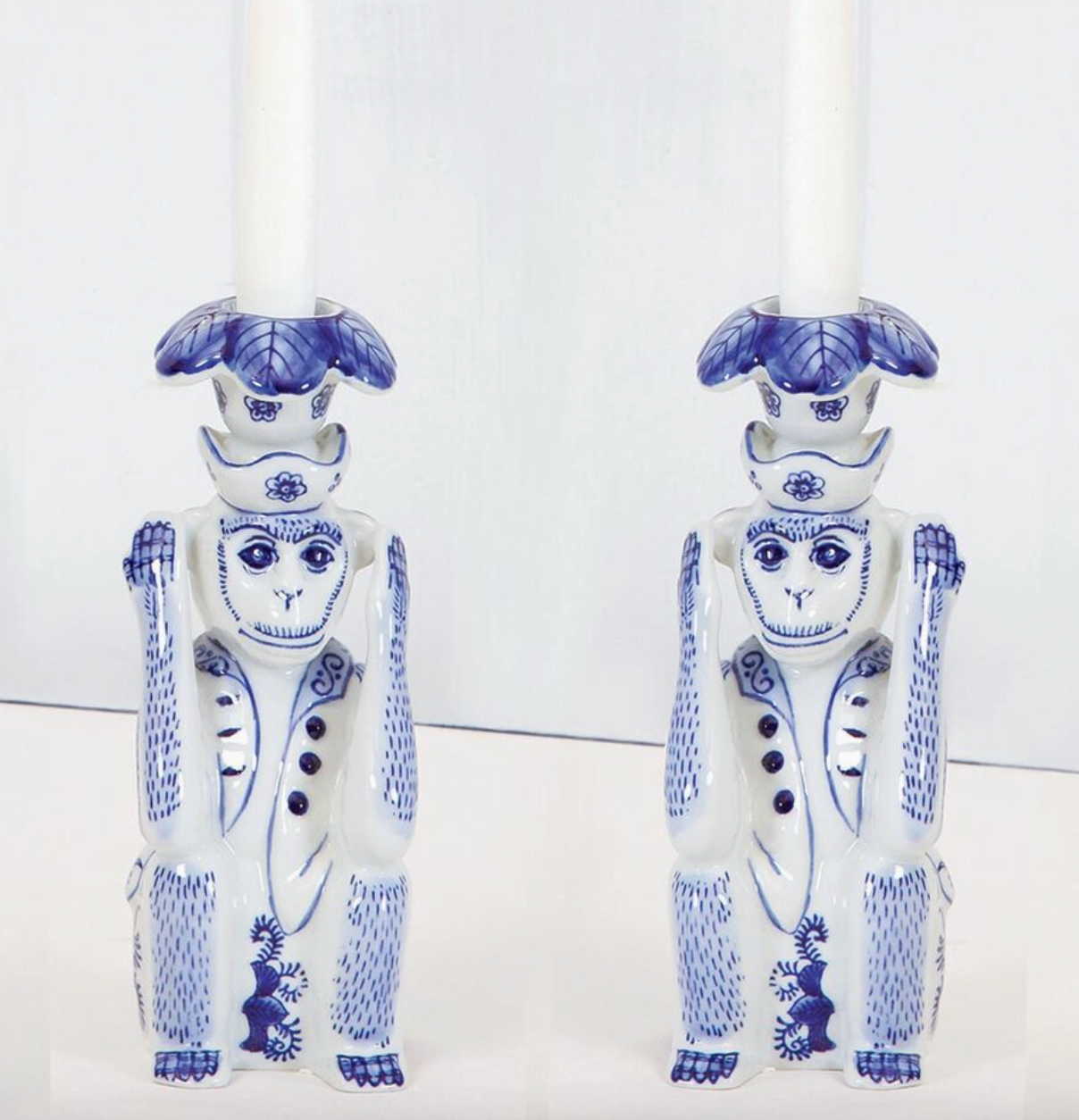 Set of Two 8 Oak Lane ceramic monkey figurine candle holders with blue and white Chinoiserie patterns with white taper candles on a white background