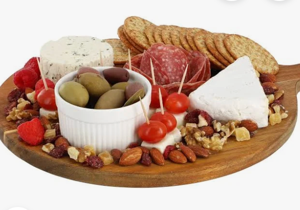 Wooden platter with assorted meats, cheeses, fruits, and nuts on a white background. Board has a handle and a hole with peg to that fits a choice of ceramic toppers for decorative addition.