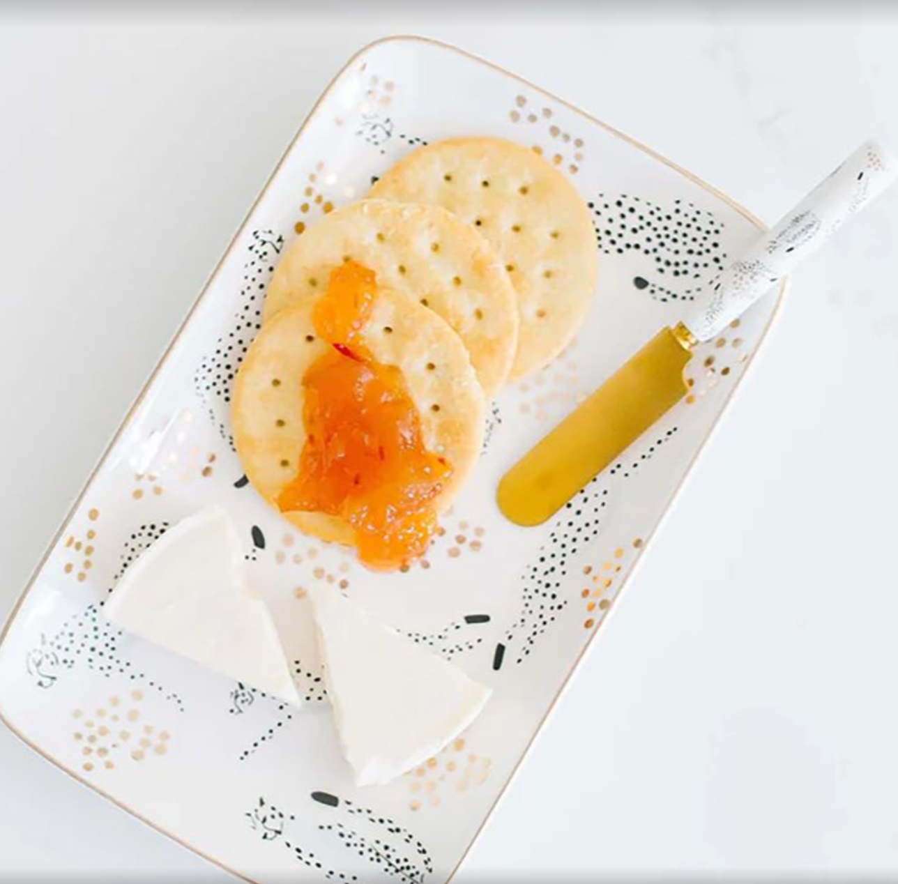 Two crackers with orange spread on a decorative gold and black cheetah printed rectangle plate with a knife