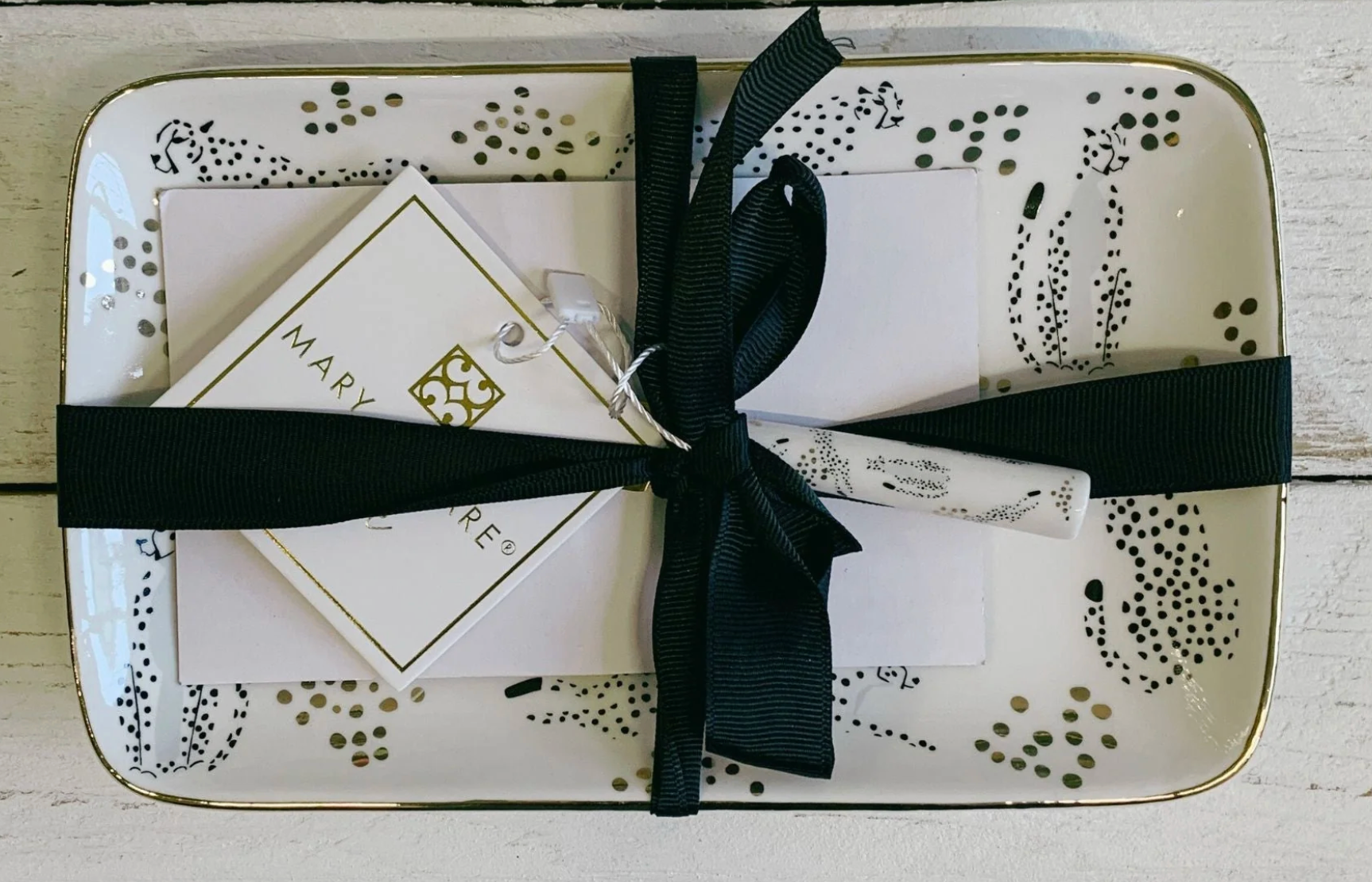 Decorative retangle tray with cheetah gold and black design with black ribbon and branded card on a wooden surface