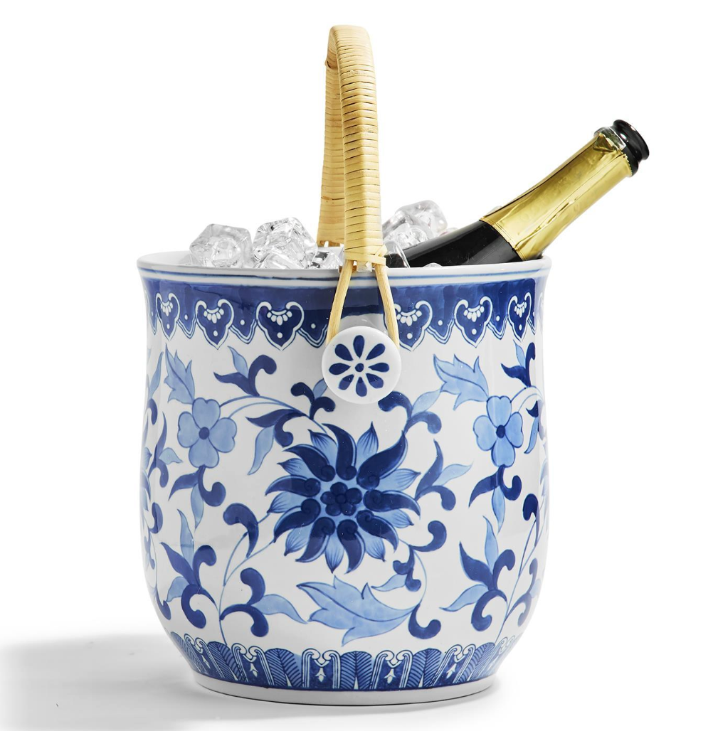 Blue and white patterned ice bucket with woven straw handle and a bottle of champagne on a white background