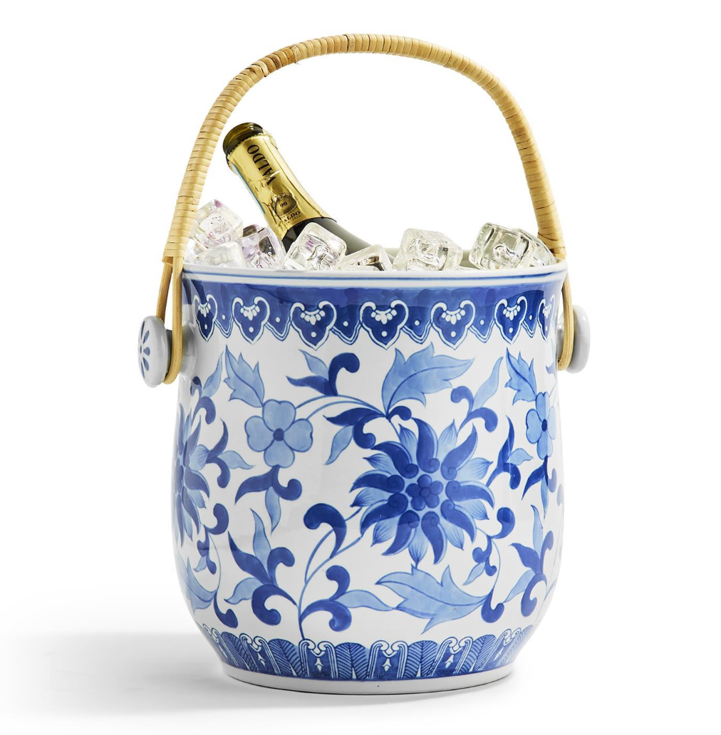 Blue and white floral-patterned ice bucket with a bottle of champagne and a rattan handle on a white background