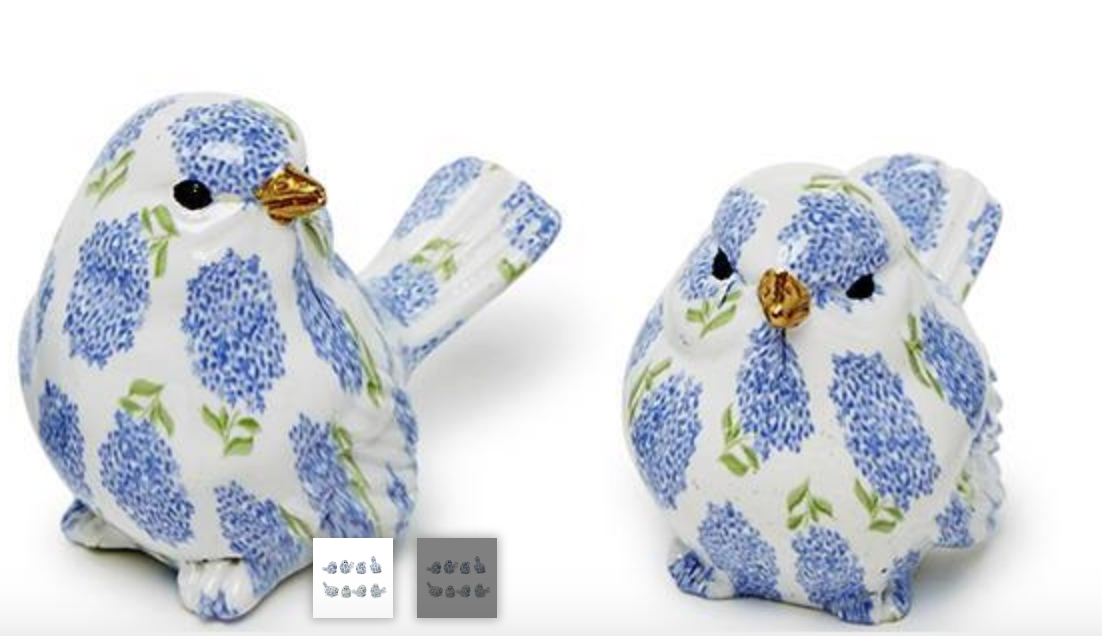 Two small bird-shaped objects with blue floral pattern and gold beaks on a white background