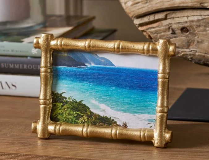 Gold bamboo picture frame on wood table with photo of ocean in the frame. Background has stacked books  