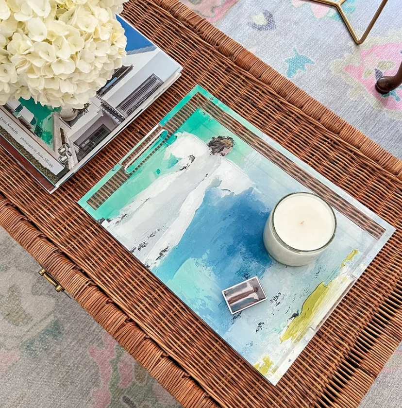 Decorative table setting with a woven brown placemat, candle, and flowers on an acrylic tray with angel on a turquoise and green bac kground