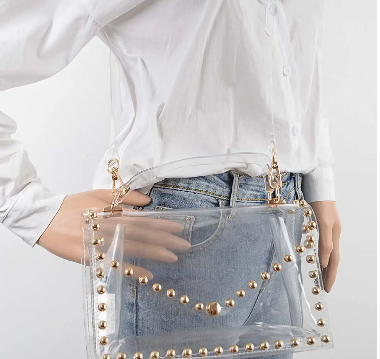 Clear bag with gold studs and gold hardware on woman with white shirt white background