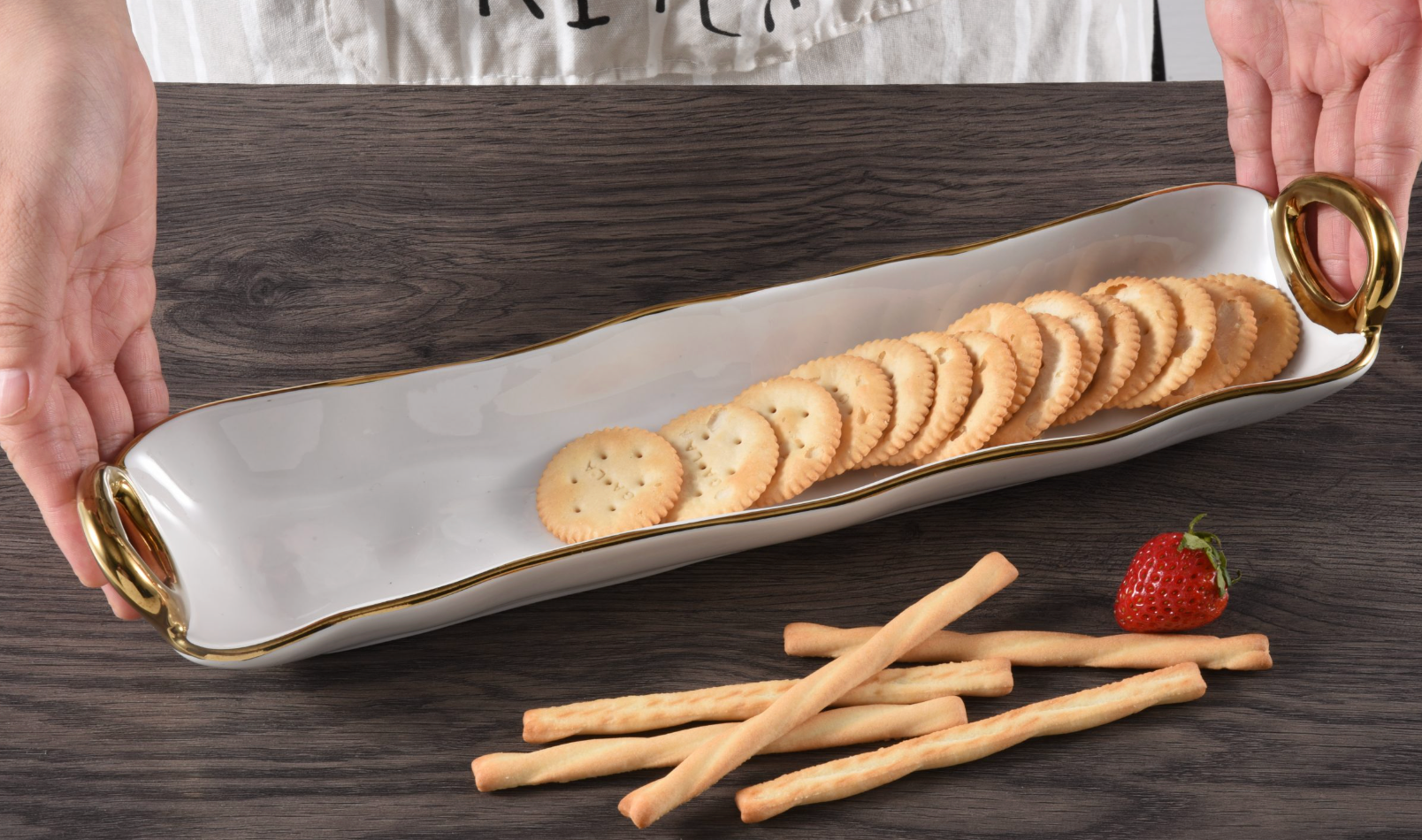 Rectangular ceramic tray with gold rim holding crackers on a wooden surface.