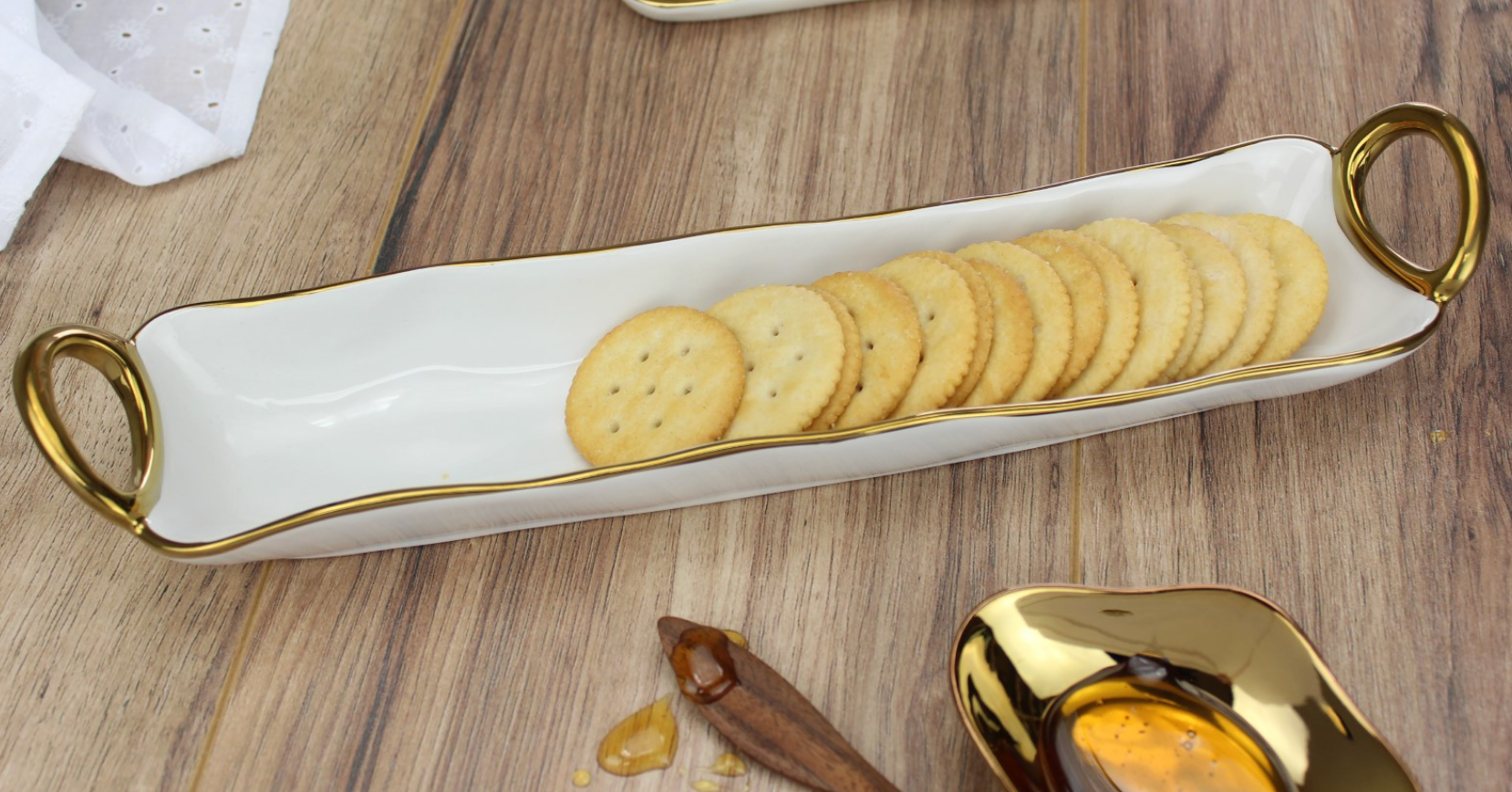 Rectangular ceramic tray with gold handles holding crackers on a wooden surface.