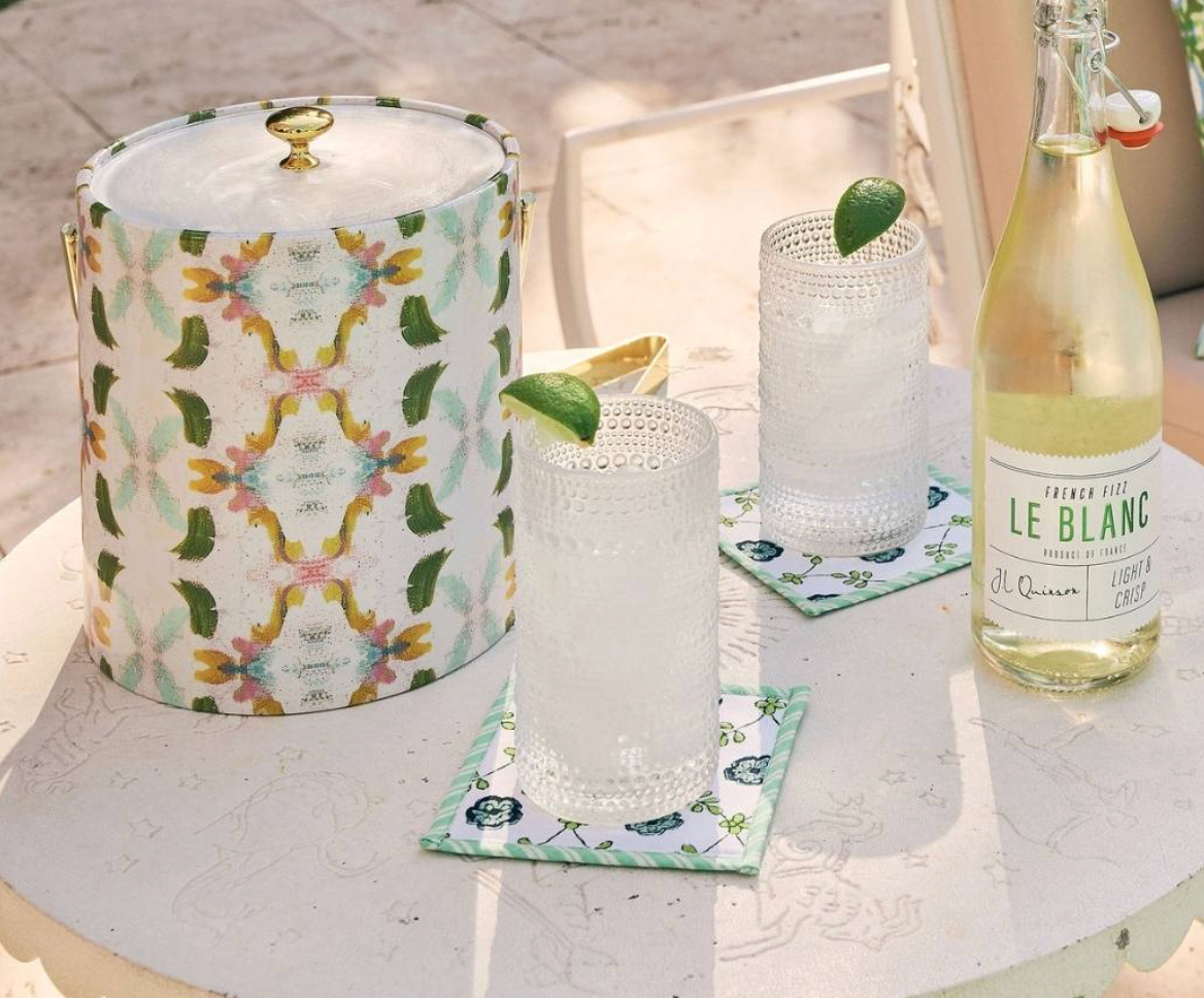 Laura Park Dogwood Decorative ice bucket with floral pattern, glasses, and a bottle of Le Blanc wine on a table.