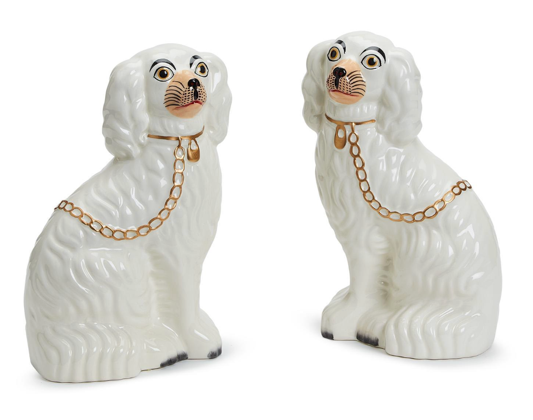 Two Staffordshire white dogs facing each other with collar and gold chain draped on their backs. 