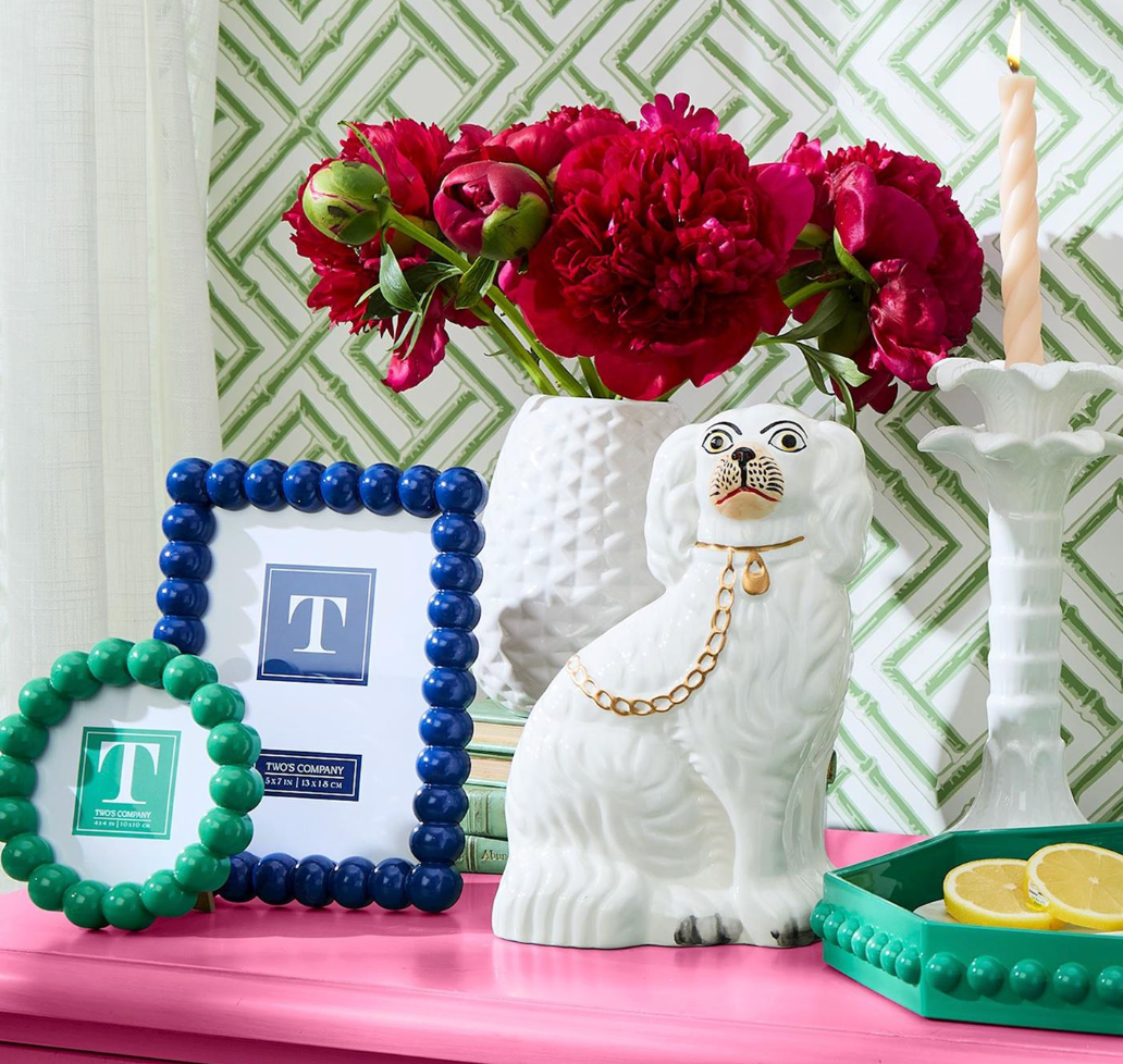 Decorative items including a white Wtaffordshire dog, blue and green picture frames, and a pink surface with flowers.