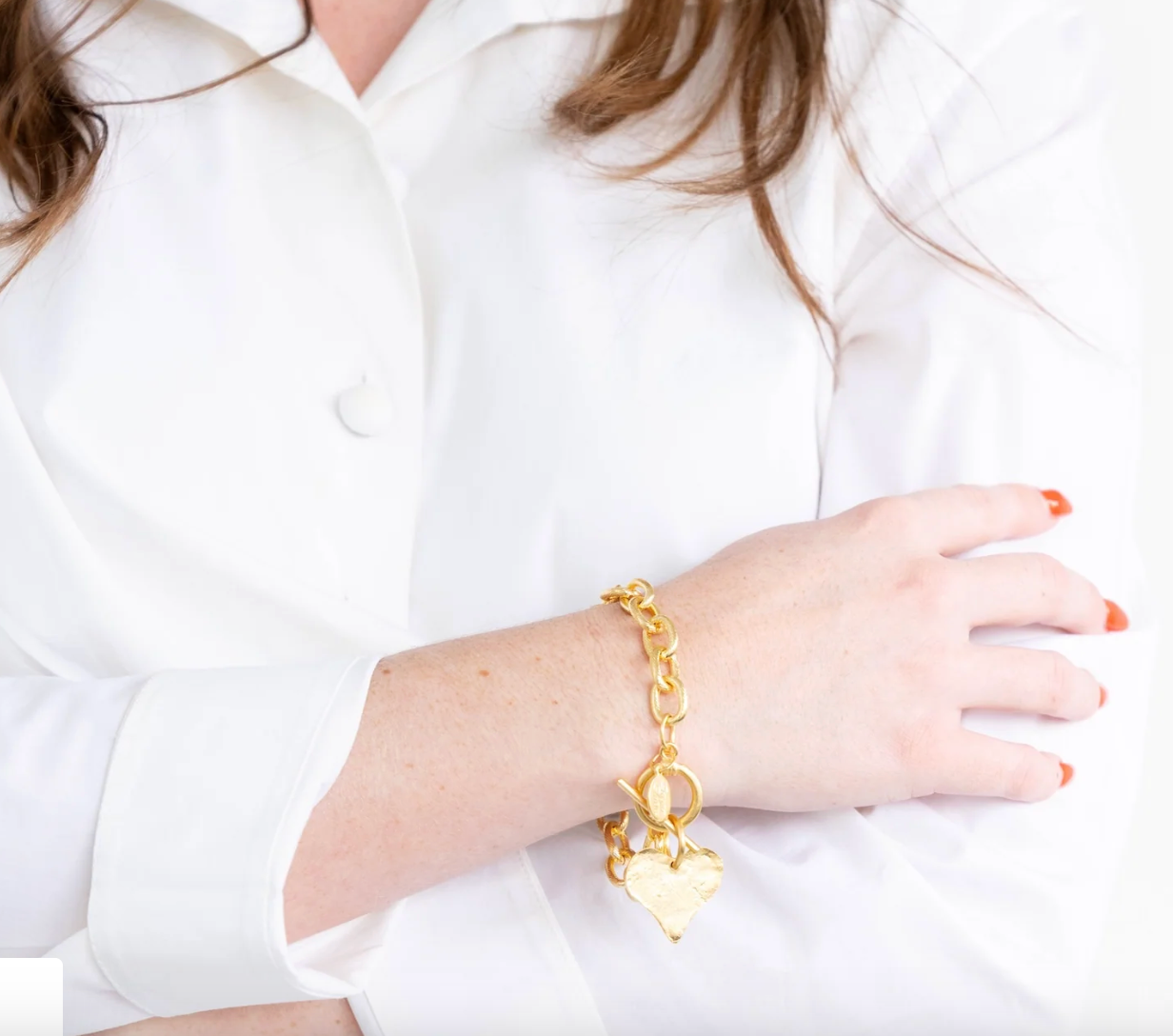 Susan Shaw Gold bracelet with a heart charm worn by a person in a white shirt.