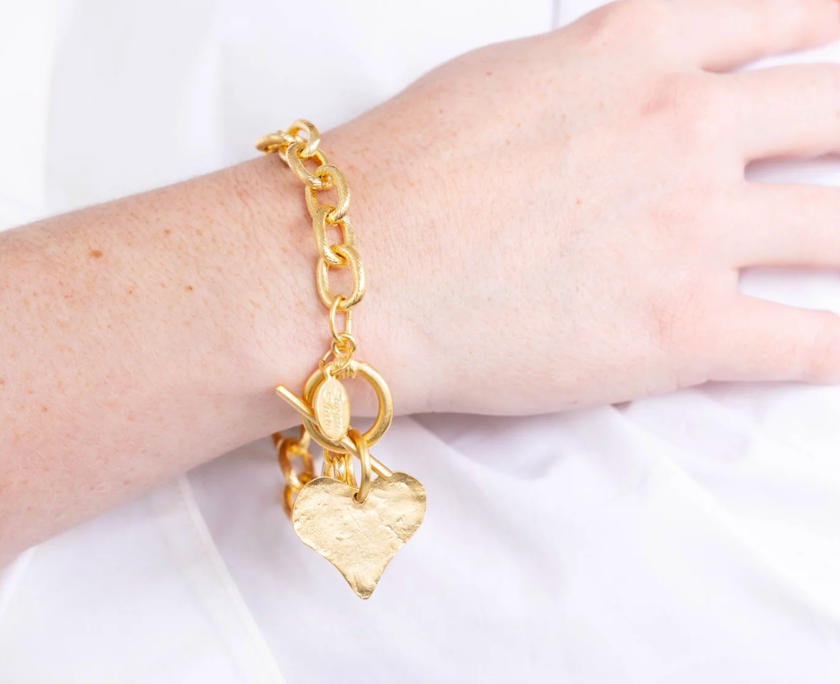 Close up of the Susan Shaw Gold bracelet with a heart-shaped charm on a white background