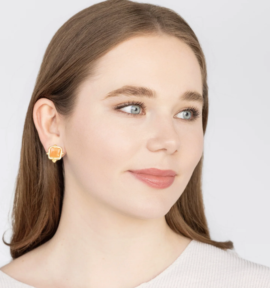 Woman wearing a pair of orange Charlotte style Susan Shaw earrings on a plain white background