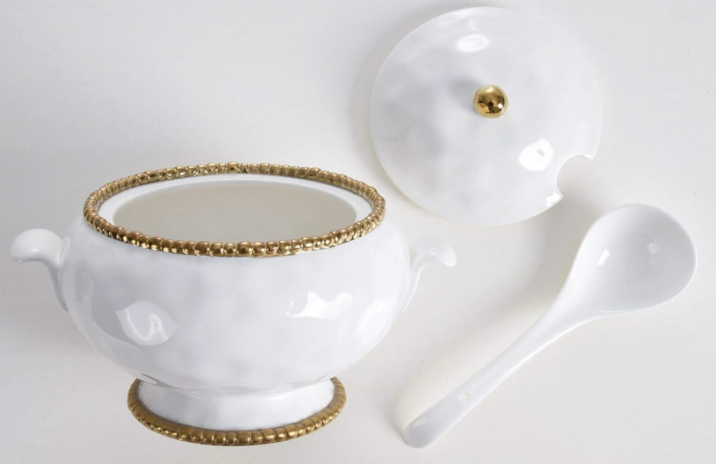 White ceramic and titanium Pampa Bay tureen, lid and spoon with gold accents on a light gray surface.